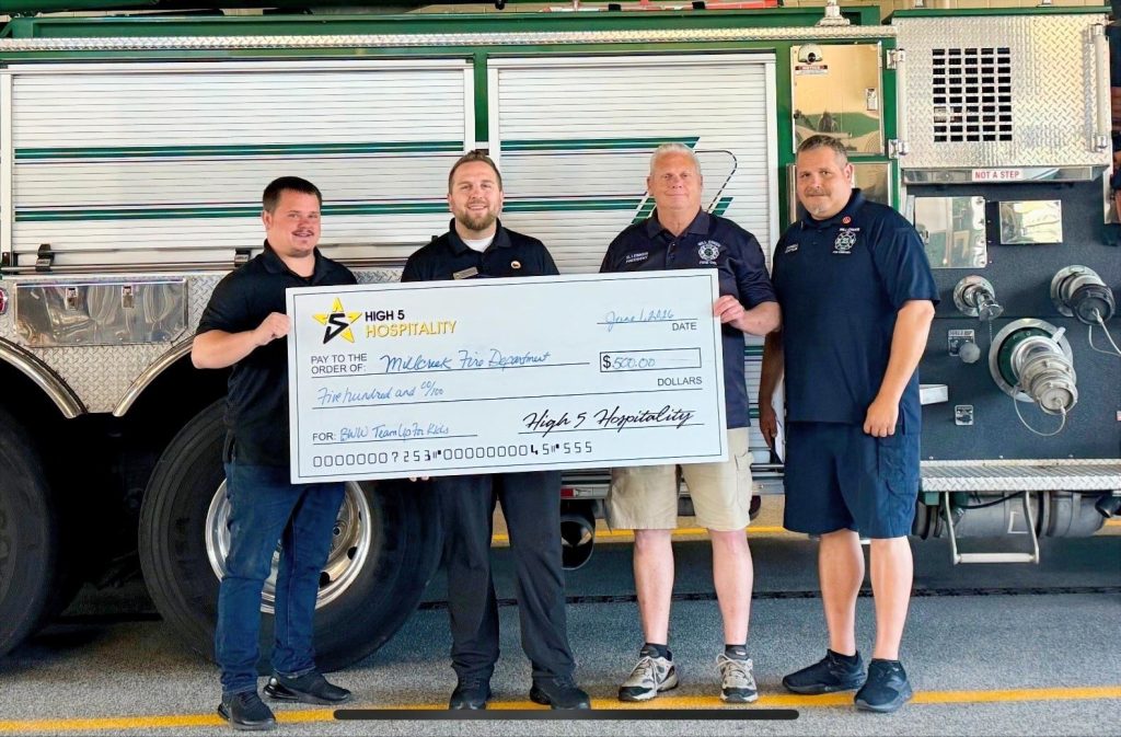 Four men stand in front of a fire truck, smiling and holding a large ceremonial check for $5,500 made out to the McCook Fire Department from High 5 Hospitality.