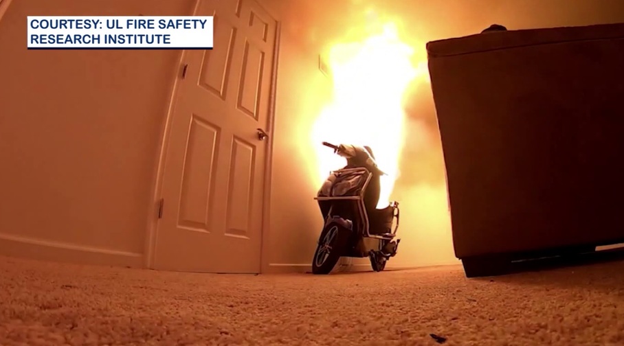 A scooter inside a room is engulfed in flames near a closed door, with smoke rising to the ceiling. Photo credit: UL Fire Safety Research Institute.